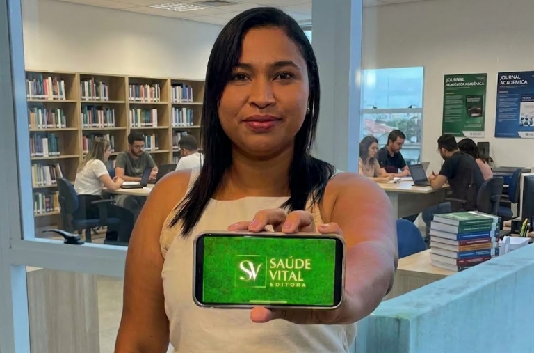 Integrante da Editora Saúde Vital mostra um celular com o logotipo da editora em uma biblioteca